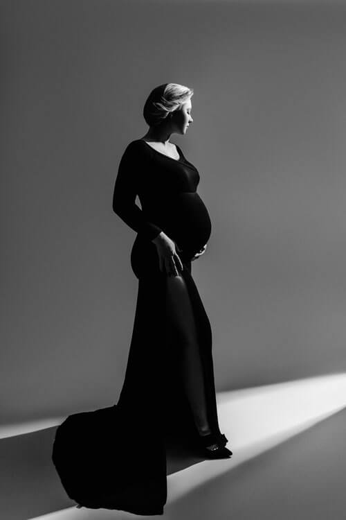 Schwarz-weißes Foto einer schwangeren Frau in einem fließenden schwarzen Kleid, die Anmut und Stärke ausstrahlt.